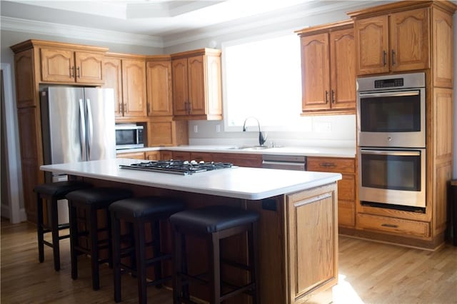 kitchen with a center island, sink, ornamental molding, appliances with stainless steel finishes, and light hardwood / wood-style floors