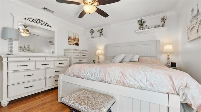 bedroom featuring crown molding, wood finished floors, visible vents, and ceiling fan