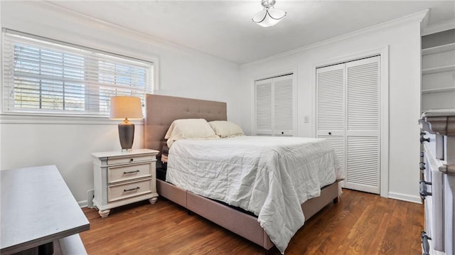 bedroom featuring crown molding, dark wood-style floors, multiple closets, and baseboards