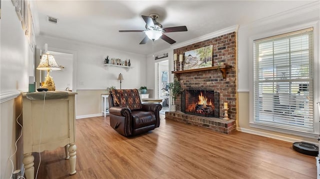 living room featuring a ceiling fan, wood finished floors, visible vents, ornamental molding, and a brick fireplace