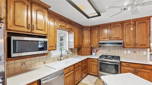 kitchen featuring appliances with stainless steel finishes, brown cabinets, under cabinet range hood, and a sink