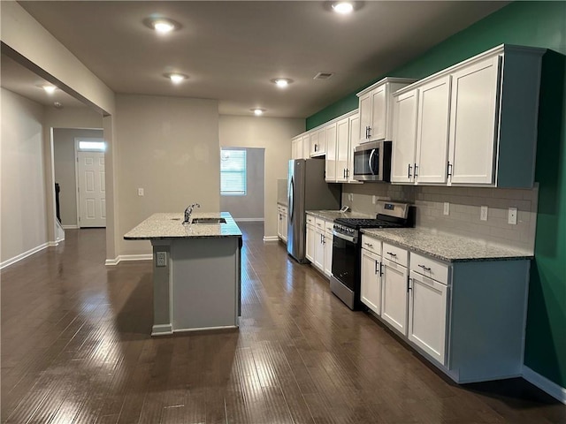 kitchen with appliances with stainless steel finishes, white cabinetry, sink, light stone countertops, and a center island with sink