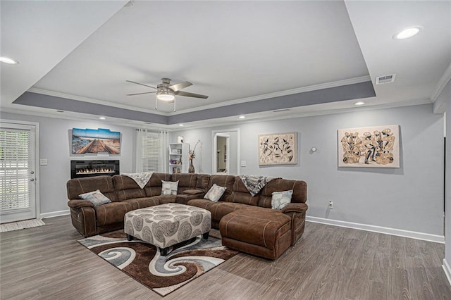 living area with a ceiling fan, a tray ceiling, crown molding, and wood finished floors