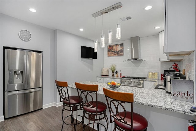 kitchen with a peninsula, visible vents, wall chimney range hood, appliances with stainless steel finishes, and tasteful backsplash