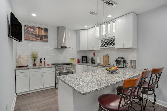 kitchen featuring a peninsula, a sink, light wood-type flooring, high end stainless steel range oven, and wall chimney range hood