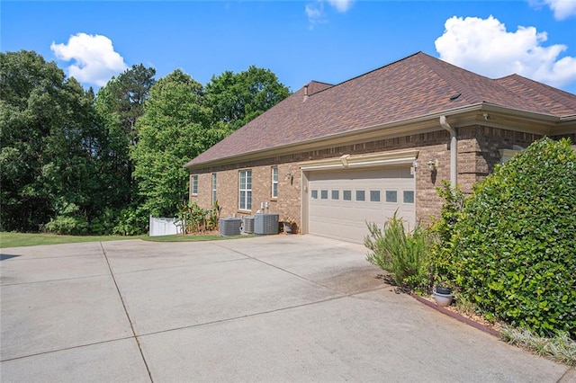 view of side of property featuring central air condition unit, brick siding, driveway, and a garage