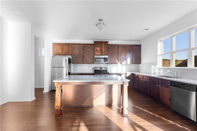 kitchen featuring stainless steel appliances, a center island, light stone countertops, decorative backsplash, and sink