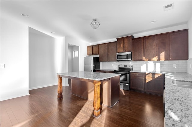 kitchen with light stone countertops, a kitchen island, tasteful backsplash, and appliances with stainless steel finishes