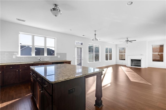 kitchen featuring sink, ceiling fan, backsplash, light stone countertops, and a kitchen island