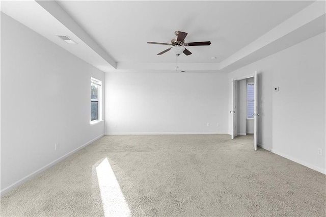 empty room with ceiling fan, a tray ceiling, and light carpet