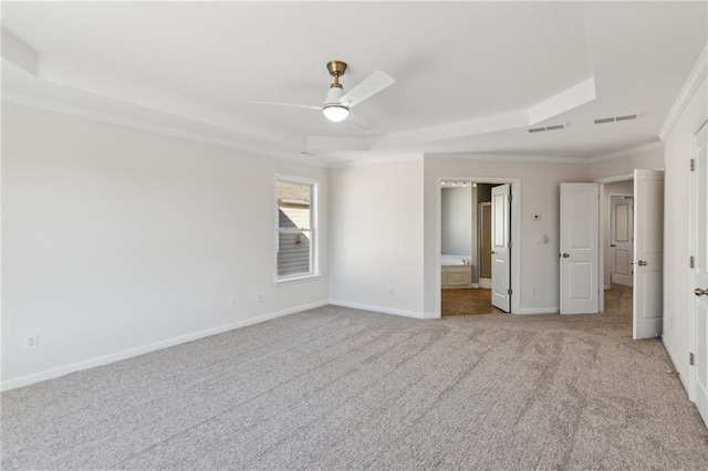 unfurnished bedroom with ensuite bathroom, ornamental molding, ceiling fan, a tray ceiling, and light carpet