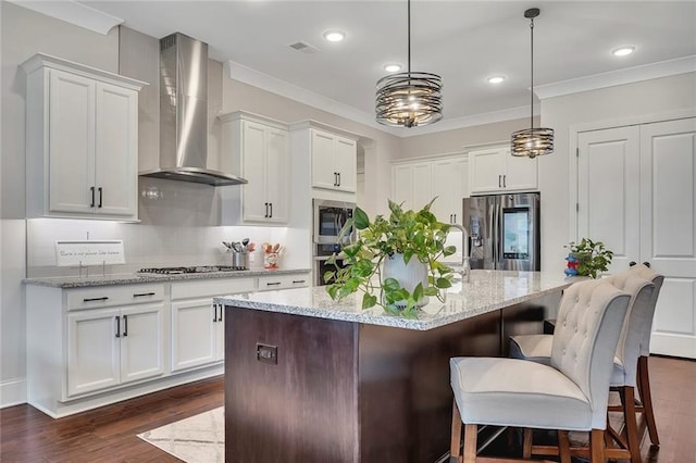 kitchen featuring wall chimney range hood, appliances with stainless steel finishes, dark wood finished floors, white cabinetry, and ornamental molding