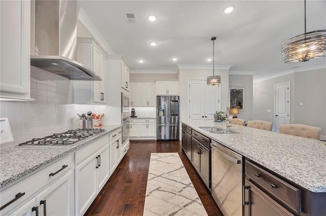 kitchen featuring stainless steel appliances, wall chimney exhaust hood, a sink, ornamental molding, and white cabinetry