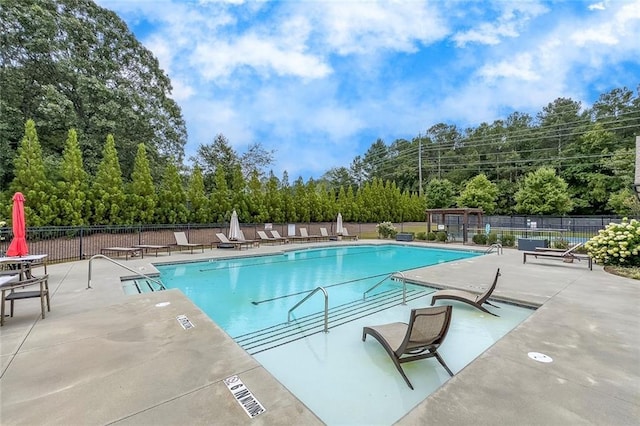 community pool with fence, a patio, and view of wooded area