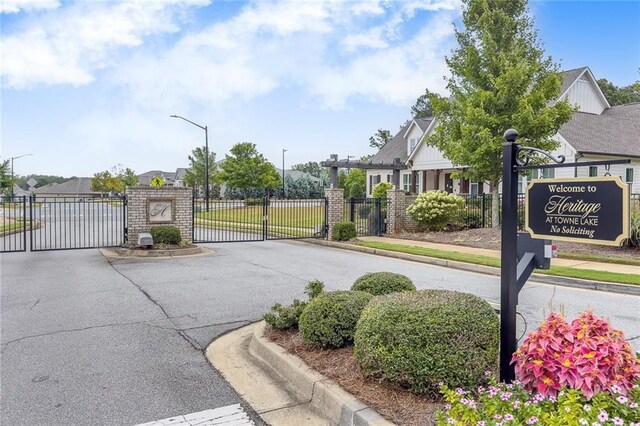 view of asphalt street with a gate, curbs, sidewalks, street lights, and a gated entry