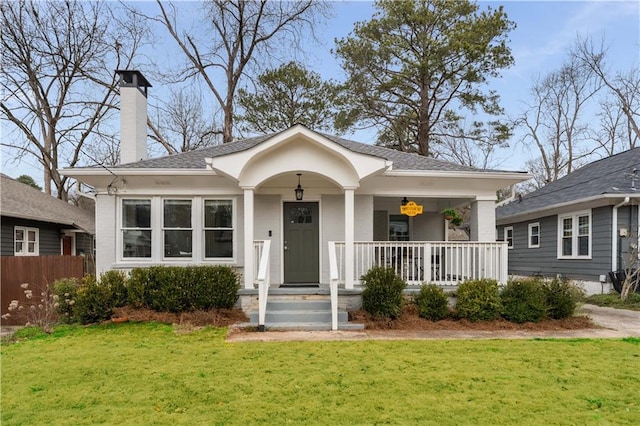 bungalow with a shingled roof, a front lawn, covered porch, and a chimney