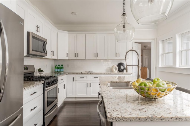 kitchen with an island with sink, ornamental molding, decorative backsplash, appliances with stainless steel finishes, and a sink