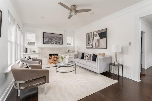 living room featuring wood finished floors, crown molding, baseboards, a brick fireplace, and ceiling fan