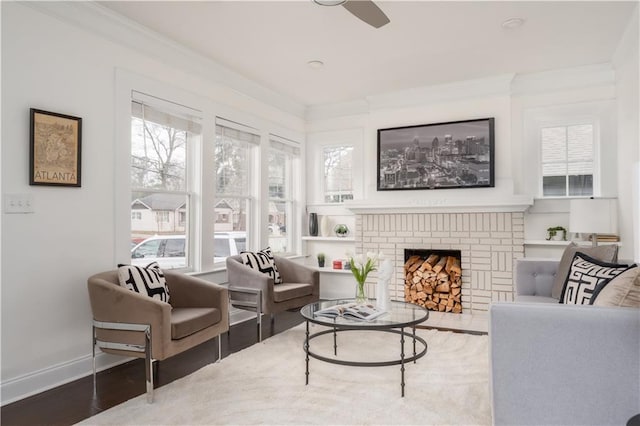 living area with wood finished floors, baseboards, ceiling fan, ornamental molding, and a brick fireplace