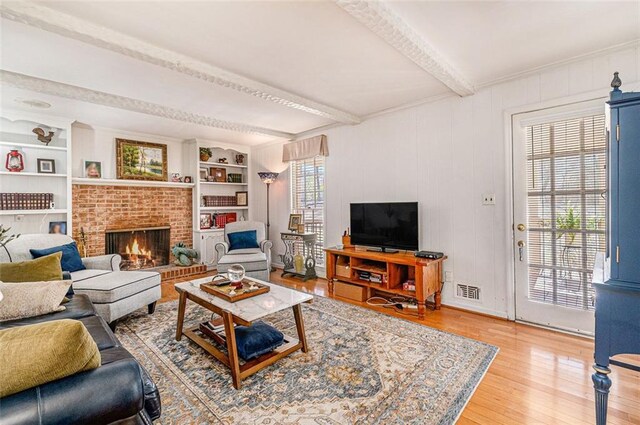 living room featuring built in features, a fireplace, visible vents, light wood-type flooring, and beamed ceiling