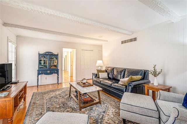 living area featuring light wood-type flooring, visible vents, and beamed ceiling