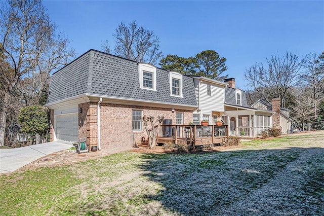 back of property with a garage, brick siding, a sunroom, a yard, and roof with shingles