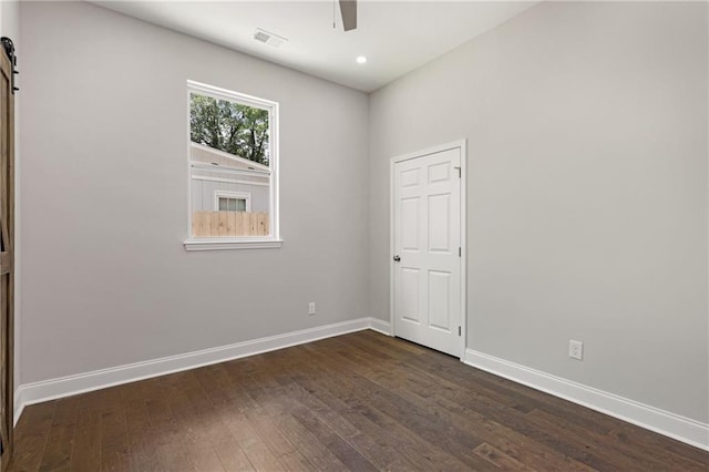 spare room with dark hardwood / wood-style flooring, ceiling fan, and a barn door