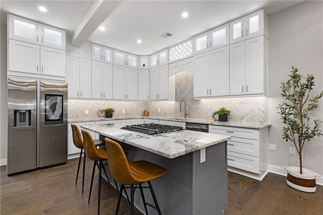 kitchen featuring stainless steel appliances, white cabinets, a center island, and light stone countertops