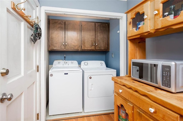 laundry room with washing machine and clothes dryer, cabinet space, and light wood-style floors