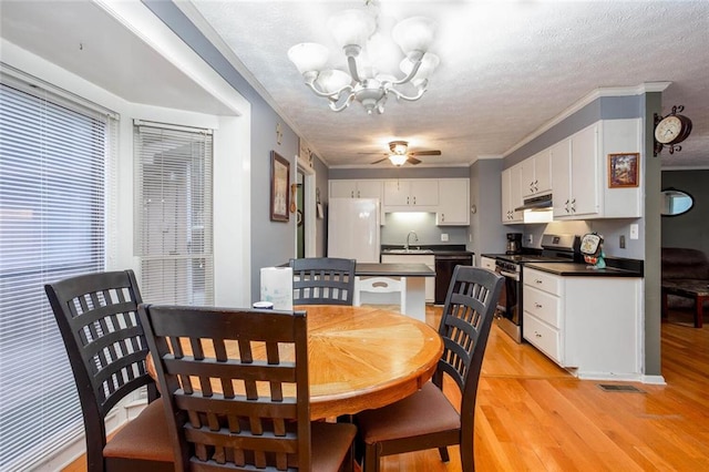 dining room featuring a chandelier, light wood-style floors, a textured ceiling, ceiling fan, and ornamental molding