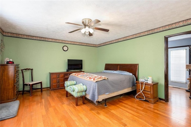 bedroom featuring wood finished floors, a textured ceiling, wallpapered walls, baseboards, and a ceiling fan