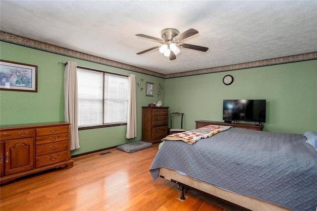 bedroom featuring wallpapered walls, light wood-style flooring, ceiling fan, and a textured ceiling