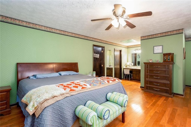 bedroom featuring wood finished floors, wallpapered walls, a textured ceiling, a ceiling fan, and ensuite bathroom