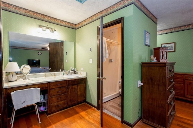 full bath with wood finished floors, wallpapered walls, a shower with curtain, vanity, and a textured ceiling