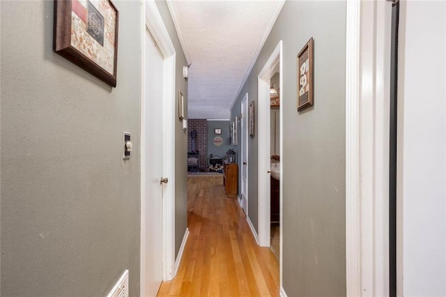 corridor featuring light wood-style floors, a textured ceiling, baseboards, and ornamental molding