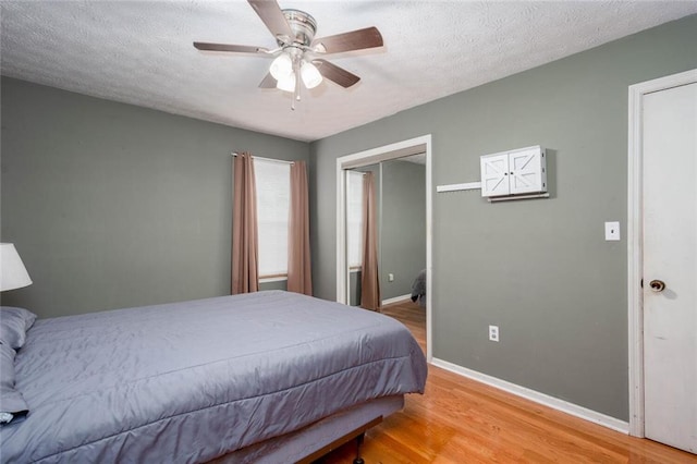 bedroom featuring light wood finished floors, baseboards, a ceiling fan, and a closet