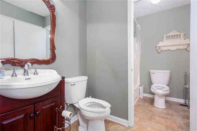 full bathroom with toilet, stone finish floors, baseboards, and vanity