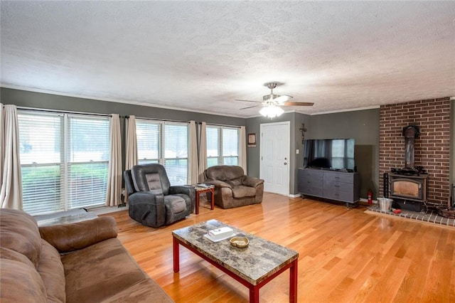 living area featuring a ceiling fan, a wood stove, a textured ceiling, and light wood finished floors