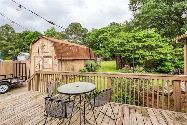 wooden terrace featuring an outbuilding, a fenced backyard, outdoor dining area, and view of scattered trees