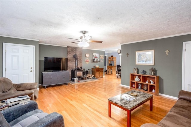 living area with a wood stove, ornamental molding, light wood-style flooring, a ceiling fan, and a textured ceiling