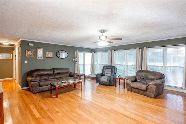 living area featuring a textured ceiling, crown molding, light wood-type flooring, a ceiling fan, and baseboards