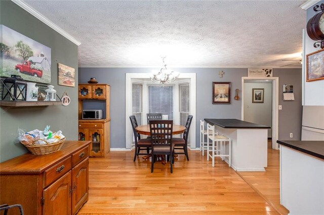dining space with a chandelier, light wood-style floors, a textured ceiling, and ornamental molding