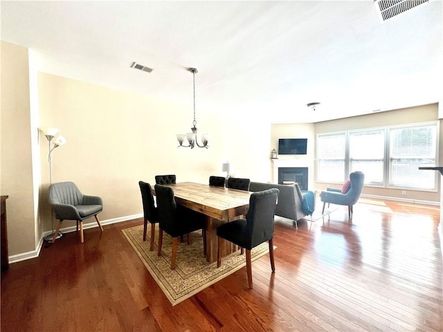 dining room featuring an inviting chandelier, a fireplace, visible vents, and wood-type flooring