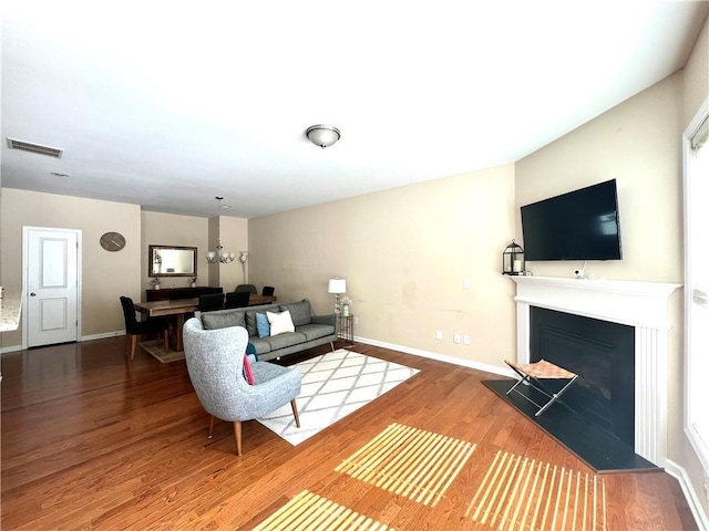 living area with visible vents, a glass covered fireplace, wood finished floors, an inviting chandelier, and baseboards