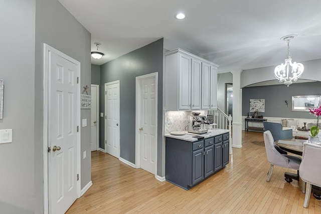 1045 Legacy Walk, Woodstock, GA 30189 - kitchen with a chandelier, light wood-style flooring, arched walkways, light countertops, and decorative backsplash