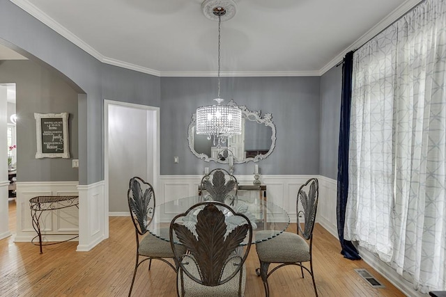 1045 Legacy Walk, Woodstock, GA 30189 - dining room with light wood finished floors, arched walkways, a chandelier, ornamental molding, and a wainscoted wall