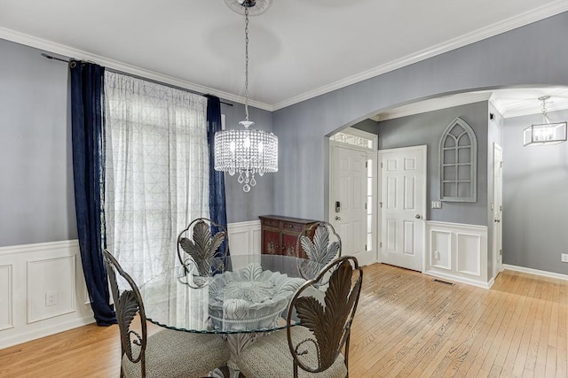 1045 Legacy Walk, Woodstock, GA 30189 - dining area featuring arched walkways, a chandelier, light wood finished floors, a decorative wall, and crown molding