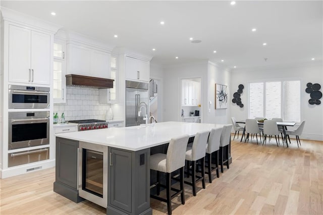 kitchen featuring white cabinetry, wine cooler, a kitchen bar, a kitchen island with sink, and appliances with stainless steel finishes