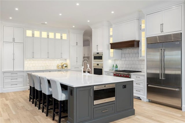 kitchen with appliances with stainless steel finishes, gray cabinetry, a breakfast bar, a kitchen island with sink, and white cabinetry