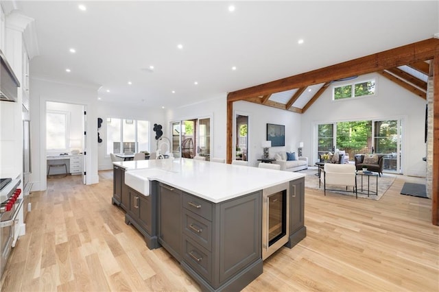 kitchen with a center island with sink, lofted ceiling with beams, sink, light hardwood / wood-style floors, and white cabinetry